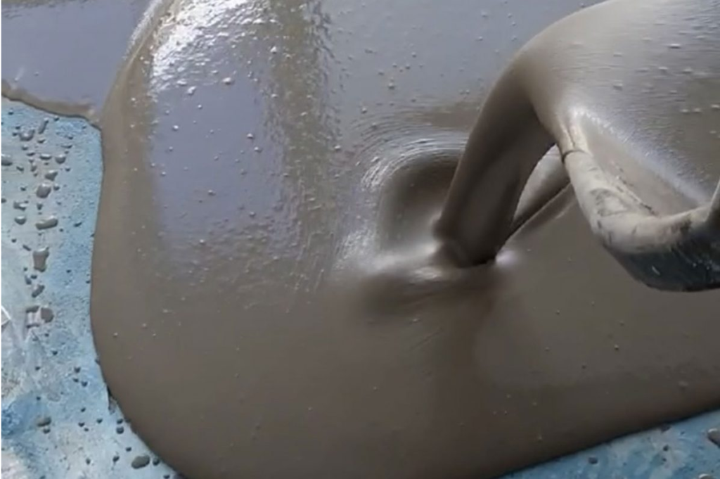A close-up of gray liquid concrete being poured, with a smooth, reflective surface.